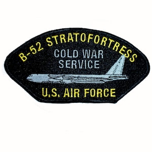 May include: A black embroidered patch featuring a light blue B-52 Stratofortress aircraft graphic. The text reads B-52 STRATOFORTRESS in yellow, COLD WAR SERVICE in white, and U.S. AIR FORCE in yellow. The patch has a curved, shield-like shape.