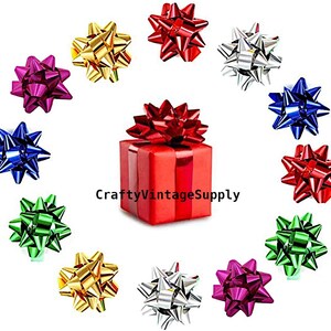 May include: An assortment of colorful gift bows in red, silver, gold, green, blue, and magenta. A red gift box is topped with a matching bow. The text "CraftyVintageSupply" is visible.