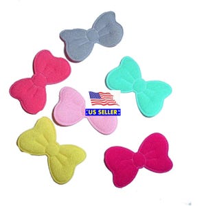 May include: Six felt fabric bows in various colors: pink, light pink, yellow, turquoise, red, and gray. The bows are all the same size and shape, and they are arranged in a circle on a white background.