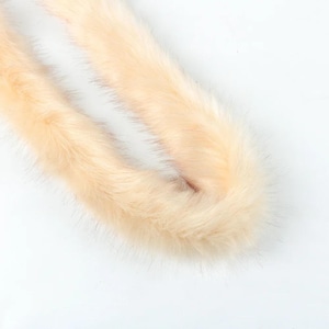 May include: A close-up shot of a pale peach-colored fur boa against a white background. The fur is soft and fluffy, with a slight sheen. The boa is curled and folded, showing its texture and color.