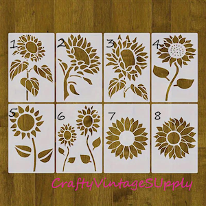 Puede incluir: Ocho plantillas de girasol diferentes, numeradas del 1 al 8, sobre un fondo de madera. Las plantillas están hechas de un material blanco y están listas para ser utilizadas en proyectos de manualidades.