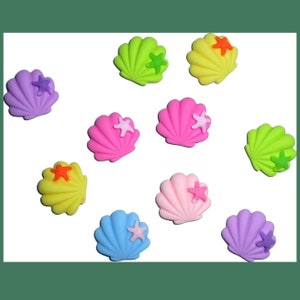 Puede incluir: Surtido de conchas de plástico de colores con detalles de estrellas de mar. Cada concha es de un color diferente, incluyendo rosa, morado, azul, verde y amarillo.