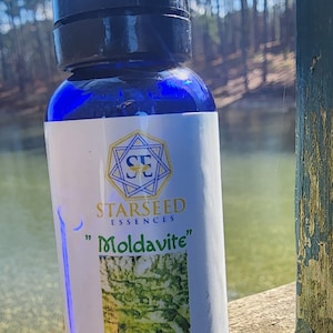 Puede incluir: Una botella de vidrio azul con tapa negra, etiquetada "Moldavita" por Starseed Essences. La etiqueta presenta una imagen verde y blanca y el texto "Tektite Essence 30 ml (Stock)".