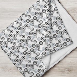 May include: A white fleece throw blanket with a pattern of gray and blue circles. The blanket is folded in half and the pattern is visible on both sides.