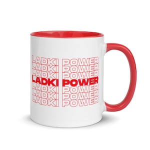 Può includere: Tazza in ceramica bianca con bordo e manico rossi. La tazza riporta le parole "Ladki Power" ripetute in rosso.