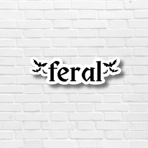 May include: A white brick wall with a black and white sticker that says "feral" with bats around the word.