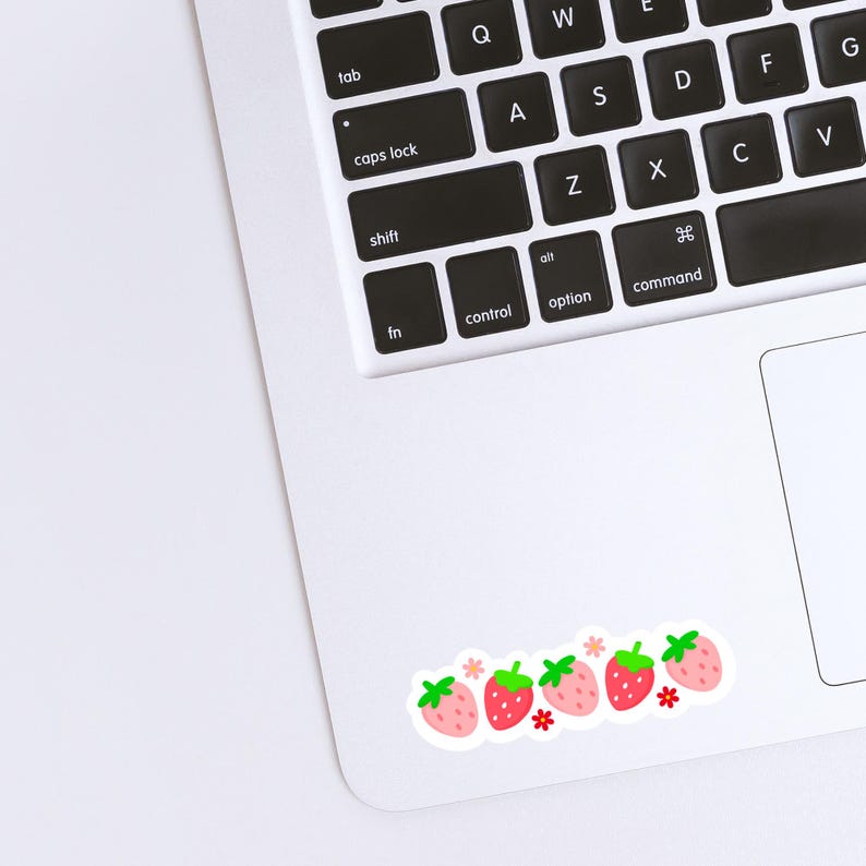 K&ouml;nnte beinhalten: Ein wei&szlig;er Laptop mit einer Reihe roter Erdbeeren mit gr&uuml;nen Bl&auml;ttern und wei&szlig;en Bl&uuml;ten auf dem Trackpad.