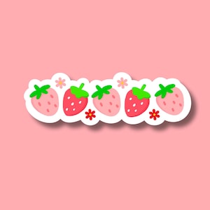 K&ouml;nnte beinhalten: Eine Reihe von f&uuml;nf roten Erdbeeren mit gr&uuml;nen Bl&auml;ttern und wei&szlig;en Bl&uuml;ten auf rosa Hintergrund.