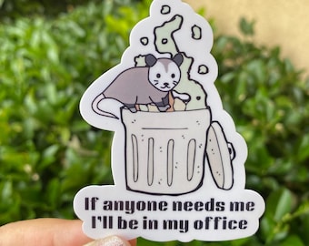 Puede incluir: Pegatina blanca con un opossum de dibujos animados en un cubo de basura. El opossum está rodeado de humo verde. El texto de la pegatina dice "Si alguien me necesita, estaré en mi oficina."