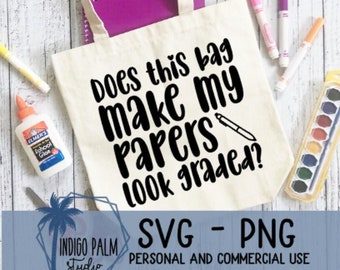 Può includere: Una borsa di tela bianca con testo nero che dice "Does this bag make my papers look graded?" La borsa è appoggiata su una superficie di legno bianco con intorno materiale scolastico.