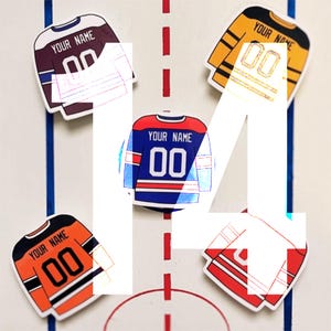 May include: Four hockey jersey stickers with the text "Your Name 00" on each. The jerseys are in different colors: maroon, yellow, blue, and red.