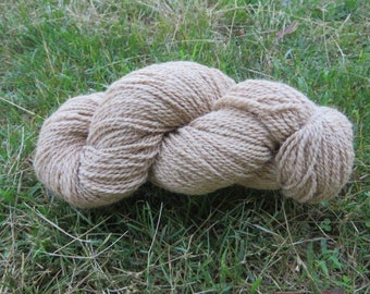 May include: A skein of light brown yarn, made from natural fibers, is lying on a bed of green grass.