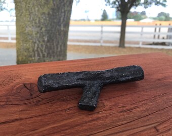 May include: A black metal T-shaped doorstop or furniture stop, sitting on a wooden surface.