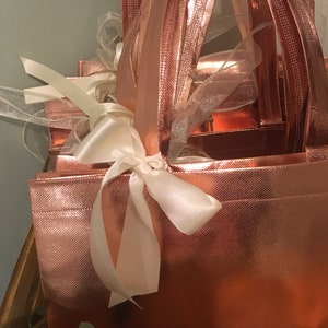 May include: A rose gold gift box set with a textured finish, tied with a white satin ribbon. The set includes multiple boxes of varying sizes, with matching rose gold handles and sheer ribbons for decoration. The overall design is elegant and festive.