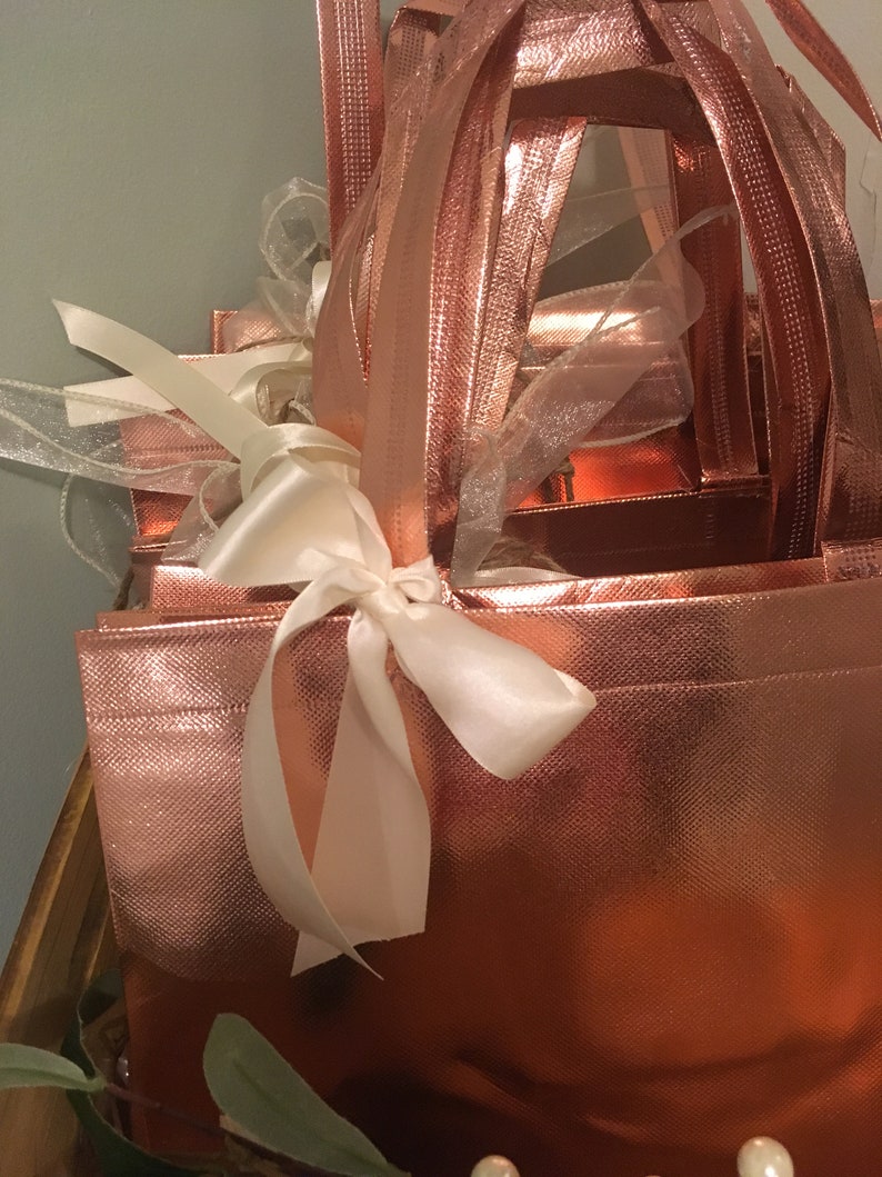 May include: A rose gold gift box set with a textured finish, tied with a white satin ribbon. The set includes multiple boxes of varying sizes, with matching rose gold handles and sheer ribbons for decoration. The overall design is elegant and festive.