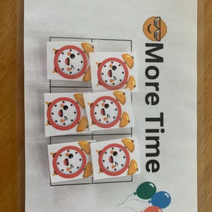 May include: A white sheet of paper with a grid of six squares. Each square contains a cartoon alarm clock with a smiling face. The text "More Time" is written vertically on the right side of the paper. There are three balloons at the bottom of the page.