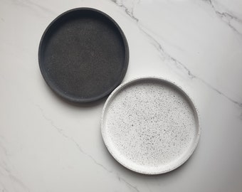 May include: Two round trays, one black and one white with a speckled pattern.