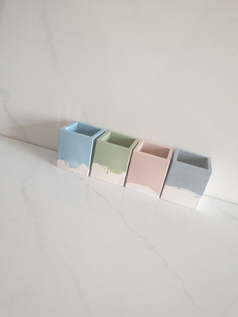 May include: Four small square concrete planters in light blue, green, pink, and gray with a white drip effect at the bottom.