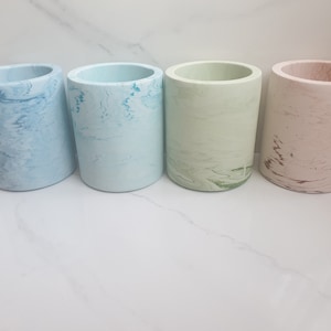 Peut inclure: Quatre pots cylindriques en béton avec un motif marbré. Les pots sont dans des tons de bleu, vert et rose.
