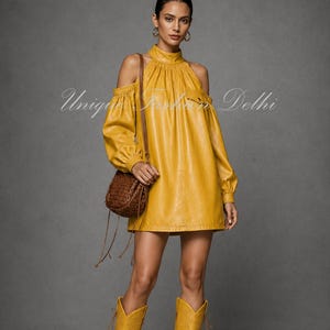May include: A mustard yellow faux leather mini dress featuring a high mock neck, cold shoulder cutouts, and long sleeves with gathered cuffs. The dress is paired with matching mustard yellow knee-high boots and a brown woven crossbody bag.