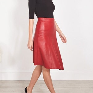 Pu&ograve; includere: Una gonna in pelle rossa abbinata a un top nero e tacchi neri. La gonna ha un design svasato e dettagli di cucitura. L'outfit &egrave; completato da tacchi neri a punta. La gonna misura circa 60 cm.
