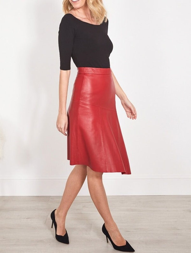 Pu&ograve; includere: Una gonna in pelle rossa abbinata a un top nero e tacchi neri. La gonna ha un design svasato e dettagli di cucitura. L'outfit &egrave; completato da tacchi neri a punta. La gonna misura circa 60 cm.