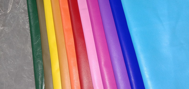 May include: A collection of colorful leather sheets in various shades, including green, yellow, orange, red, pink, purple, and blue. The sheets are arranged side by side, showcasing a spectrum of colors and textures, suitable for crafting.