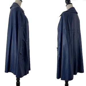 May include: A navy blue cape with a collar and a long, flowing silhouette. The cape is made of a smooth, textured fabric and has a simple, elegant design.