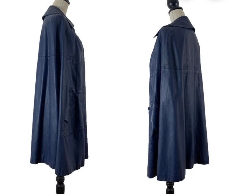 May include: A navy blue cape with a collar and a long, flowing silhouette. The cape is made of a smooth, textured fabric and has a simple, elegant design.