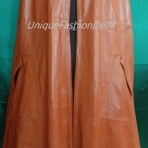 May include: A brown leather cape with a high collar and a button closure. The cape has two pockets on the sides and a long, flowing design. The text "UniqueFashionDelhi" is visible on the front of the cape.
