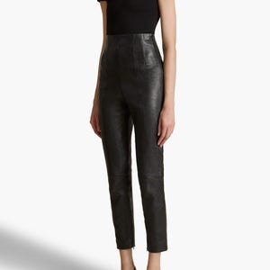 May include: A black outfit comprising a short-sleeved top and high-waisted leather trousers. The trousers have a tailored fit, and the outfit is completed with black heeled loafers. The ensemble presents a sleek, modern appearance.