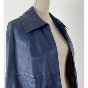 May include: A navy blue leather jacket with a long, fitted silhouette and a large collar. The jacket has a single-breasted closure and a smooth, polished finish.