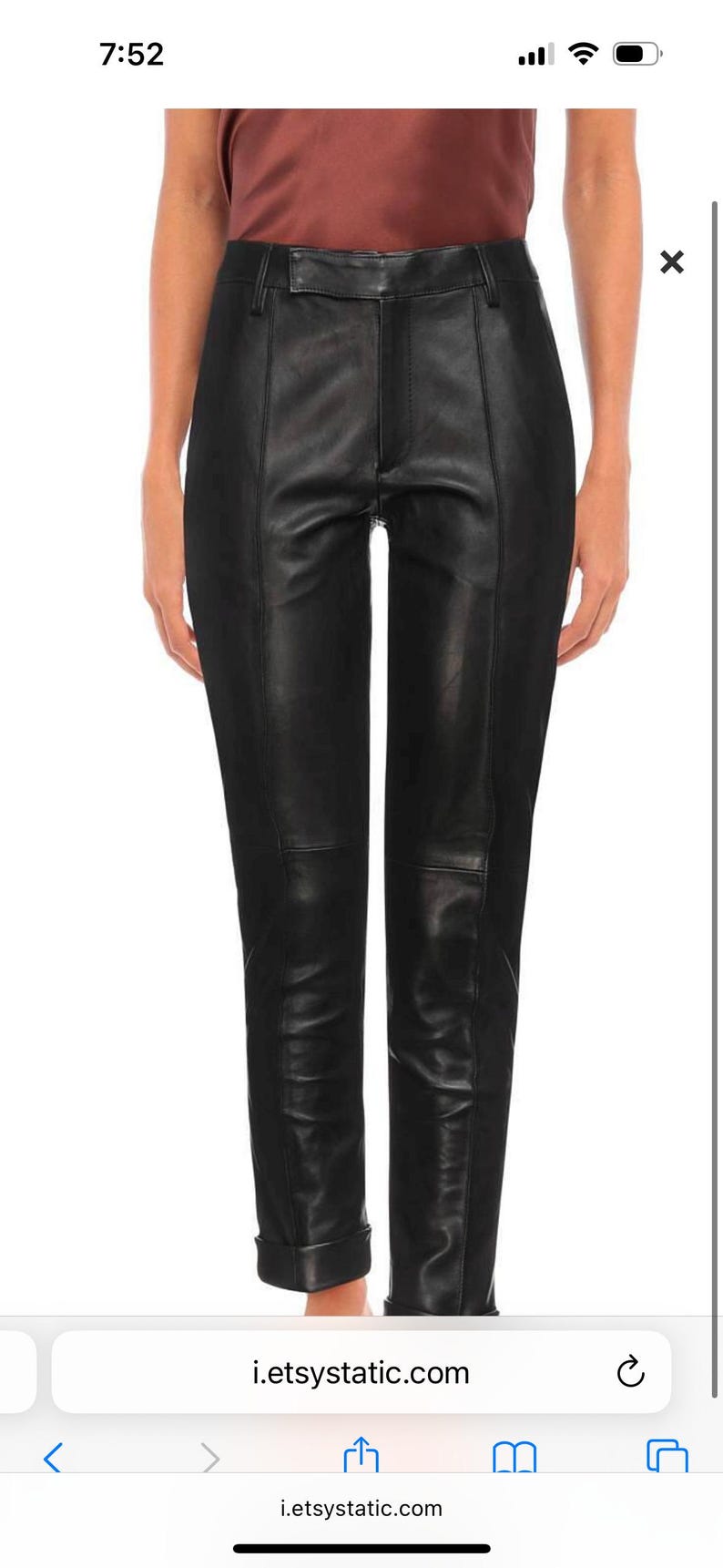May include: Black leather pants with a tailored fit. The pants have a high waist, a seam down the front of each leg, and are cuffed at the ankles. The pants are made of a smooth, shiny leather material.