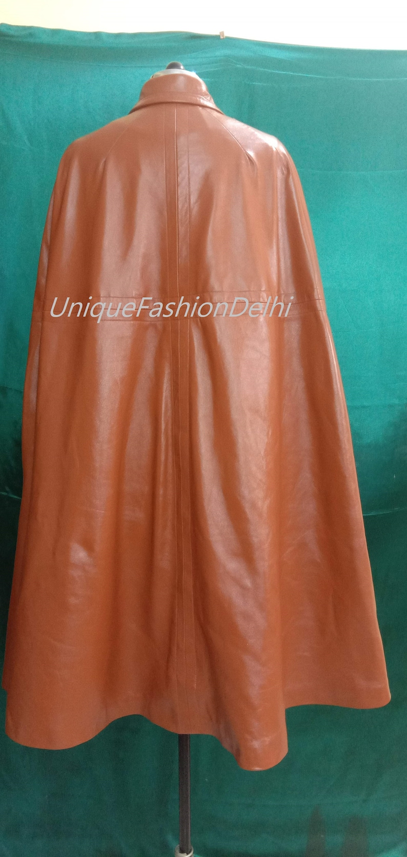May include: A brown leather cape with a collar and a seam down the back. The cape is on a mannequin against a green background. The text "UniqueFashionDelhi" is printed on the cape.