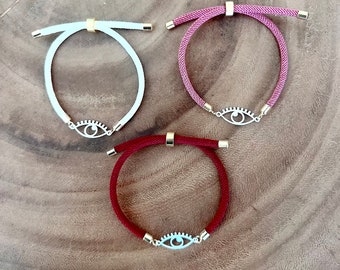 May include: Three bracelets with an evil eye charm. The bracelets are made of cord and come in white, pink, and red.
