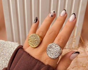 May include: Two silver rings with intricate designs. The rings are round and have a raised design that looks like Arabic script. The rings are on a person's finger.