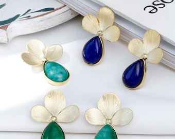 May include: A pair of gold flower-shaped earrings with teardrop-shaped blue and green gemstones. The earrings are on a white surface.
