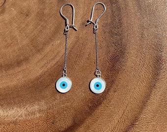 May include: A pair of silver earrings with a blue and white evil eye charm hanging from each earring.