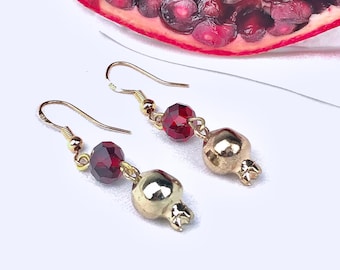 May include: Gold pomegranate earrings with red crystal beads. The earrings are dangling and have a hook closure.