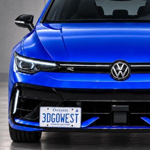 Puede incluir: Un coche hatchback Volkswagen de color azul brillante visto desde el frente, con techo negro, espejos laterales negros y parachoques delantero negro. El vehículo muestra una matrícula de Ontario con el texto 3DGOWEST y una insignia R en la rejilla.