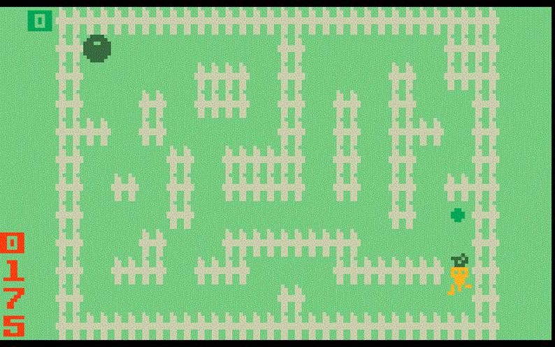 May include: A retro video game screen with a green background and white picket fences forming a maze. A green ball, a green dot, and a carrot-like figure are visible. The score is displayed in red.