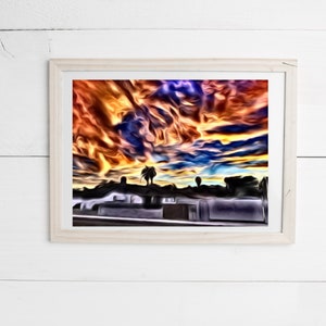 May include: Abstract art print in a light wood frame. The artwork depicts a vibrant, stylized sunset with fiery orange, yellow, and blue hues. Silhouetted figures stand on a rooftop, adding a sense of scale and mystery to the scene.