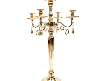 May include: A gold metal candelabra with five candle holders and crystal drop accents. The candelabra has a tall, ornate base and a decorative design.