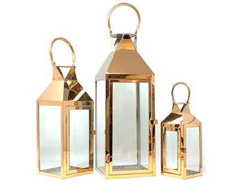 May include: Three gold metal lanterns of different sizes with glass panels. The lanterns have a simple, modern design and would be a stylish addition to any home decor.