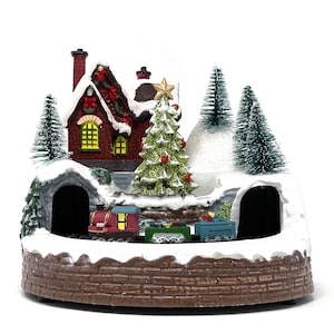 May include: A Christmas village scene with a red brick house, a green Christmas tree, and a train traveling around a snowy landscape. The house has a red roof and white trim, and the train is pulling a red caboose and several other cars.