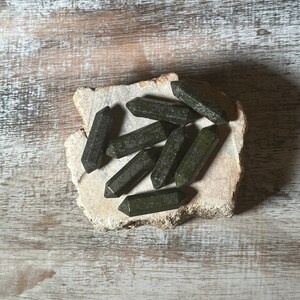 May include: A group of dark green, pointed crystal stones on a light brown wooden surface.