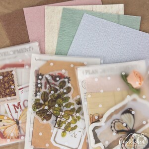 May include: Three clear plastic bags with white polka dots, each containing various paper ephemera, including vintage-style stamps, floral illustrations, and a butterfly sticker. The bags are arranged on a brown surface.