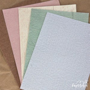 May include: Five sheets of textured paper in different colours: brown, pink, beige, green, and light grey. The paper is arranged in a fan shape, with the brown sheet at the bottom and the light grey sheet at the top.