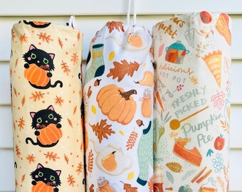 May include: Three reusable grocery bags with fall-themed designs. The first bag has a yellow background with black cats holding pumpkins. The second bag has a white background with pumpkins, pears, leaves, and jars. The third bag has a white background with a pumpkin pie, apples, and the text "Farmers Market" and "Freshly Picked Pumpkin Pie".
