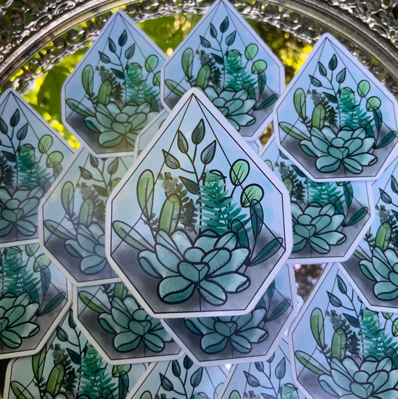 以下が含まれることがあります： 緑色の植物と多肉植物が描かれた幾何学的なテラリウムのデザインのステッカー10枚セット。ステッカーは、青い色合いの白い背景に印刷されています。